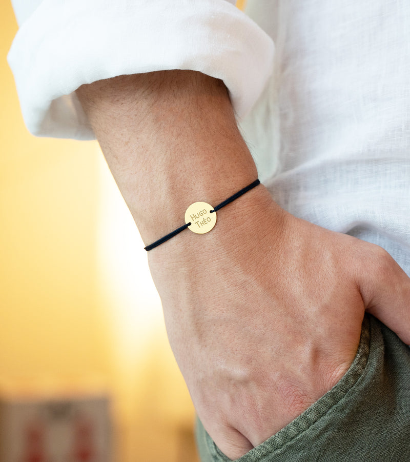 bracelet en plaqué or avec une médaille personnalisée de 15mm avecdeux trous et un cordon noir incarne l'élégance.