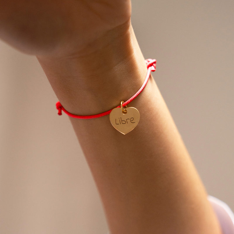Sur fond orange fluo, un bracelet cœur personnalisé de 15mm en plaqué or brille avec élégance, souligné par un cordon vif.