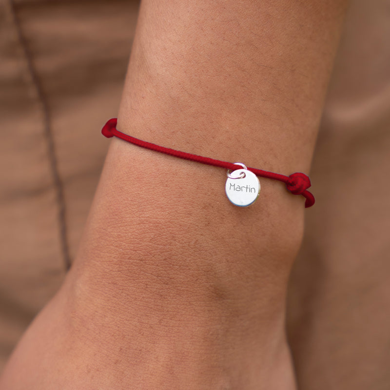 Un bracelet argenté orné d'une médaille de 10mm et d'un cordon rouge, personnalisable.