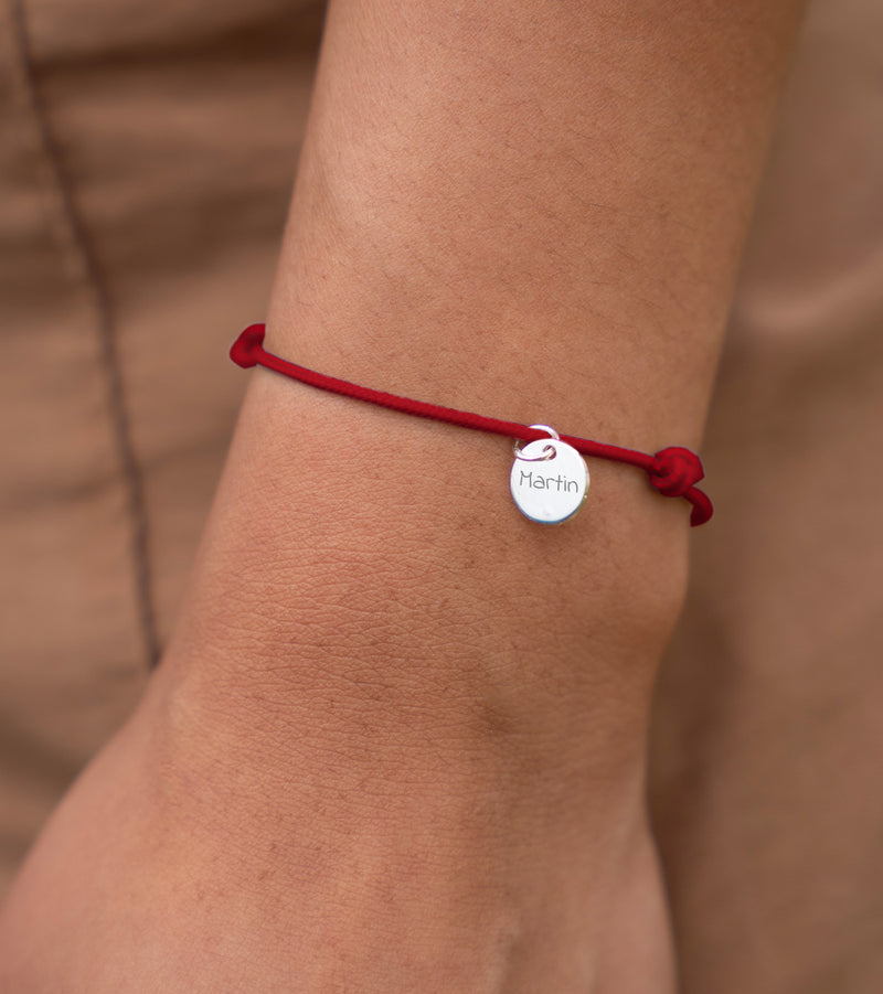 Un bracelet argenté orné d'une médaille de 10mm et d'un cordon rouge, personnalisable.