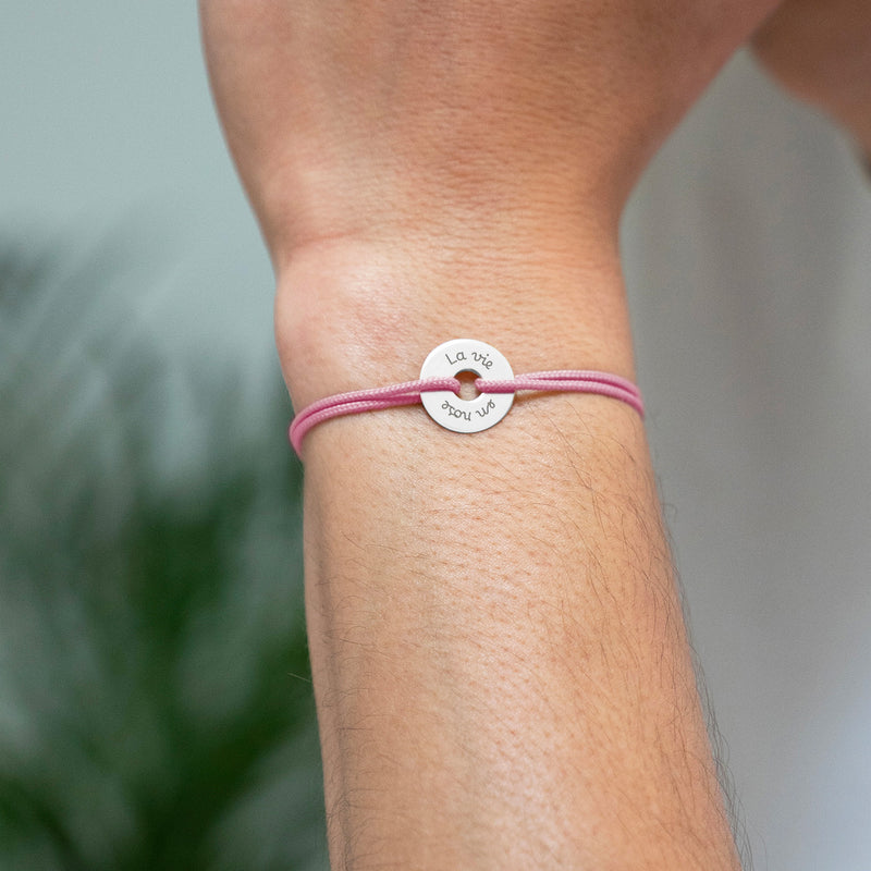 Arborant un cordon rose, ce bracelet en forme de cible est personnalisé de 15mm en argent.