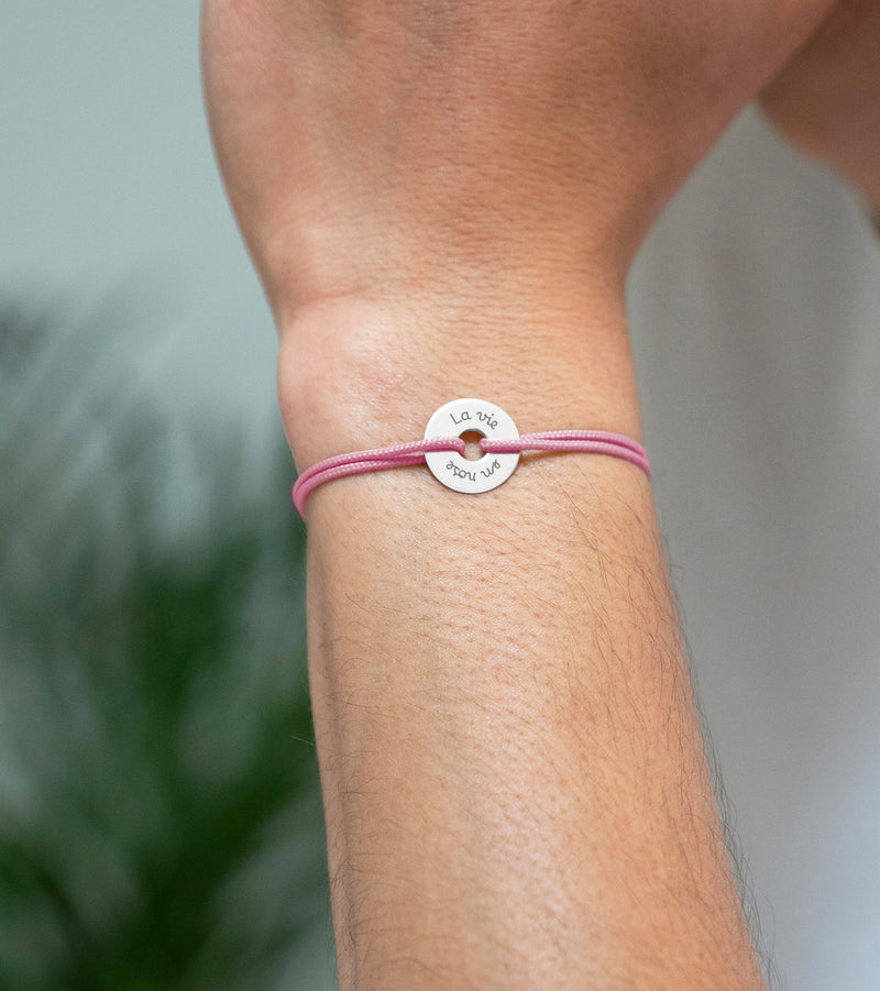 Arborant un cordon rose, ce bracelet en forme de cible est personnalisé de 15mm en argent.