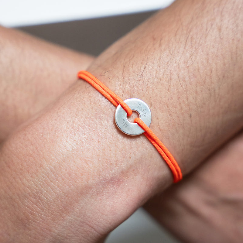Arborant un cordon orange fluo, ce bracelet en forme de cible est personnalisé de 15mm en argent.
