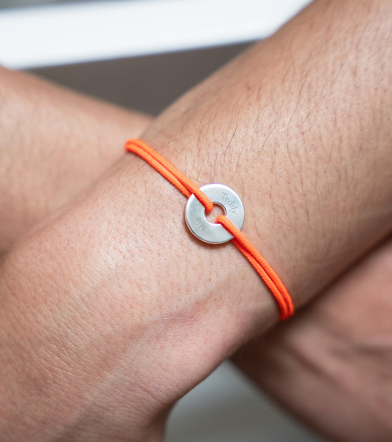 Arborant un cordon orange fluo, ce bracelet en forme de cible est personnalisé de 15mm en argent.
