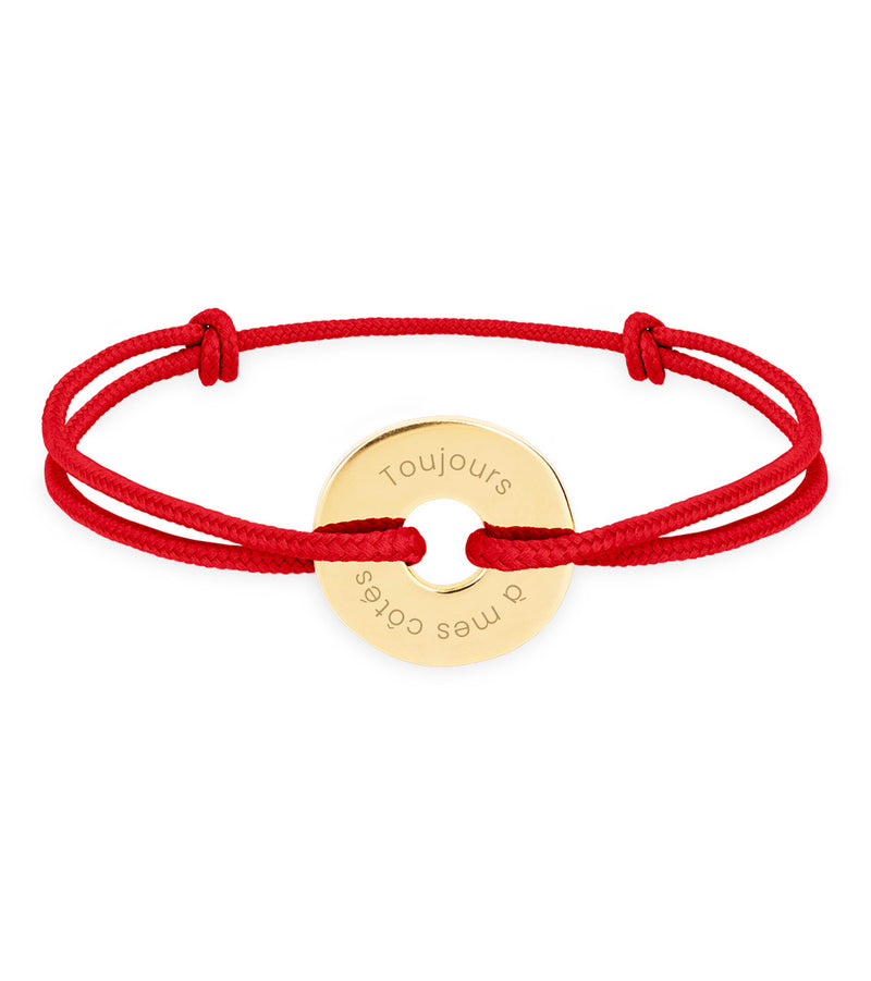 Un bracelet en forme cible, personnalisé en 15mm, plaqué or, agrémenté d'un cordon rouge.