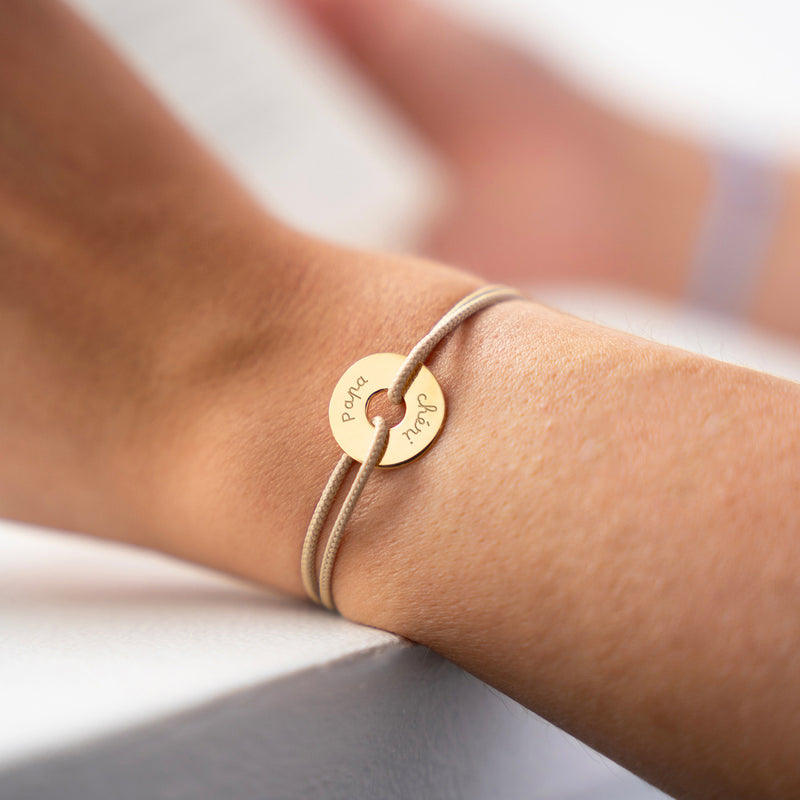 Le bracelet plaqué or, personnalisé en 15mm, se distingue par sa forme cible et son cordon beige.