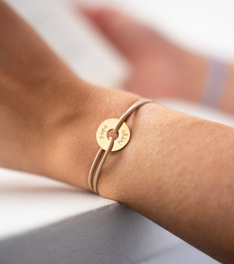 Le bracelet plaqué or, personnalisé en 15mm, se distingue par sa forme cible et son cordon beige.
