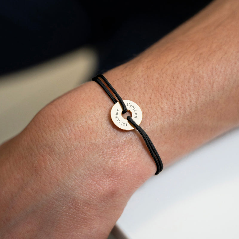 Avec une forme cible, ce bracelet personnalisé en 15mm, plaqué or, est agrémenté d'un cordon noir.