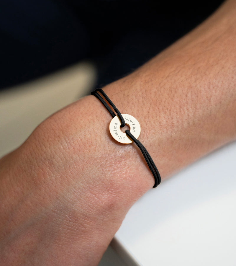 Avec une forme cible, ce bracelet personnalisé en 15mm, plaqué or, est agrémenté d'un cordon noir.