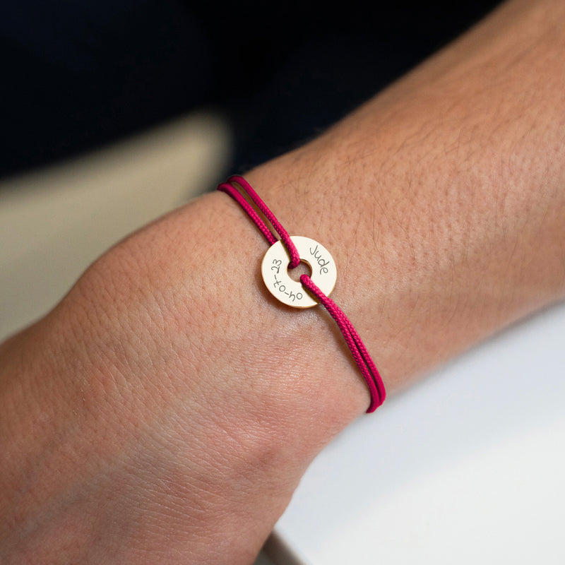 Le bracelet personnalisé en 15mm, plaqué or, forme cible, est complété par un cordon rose fuchsia.