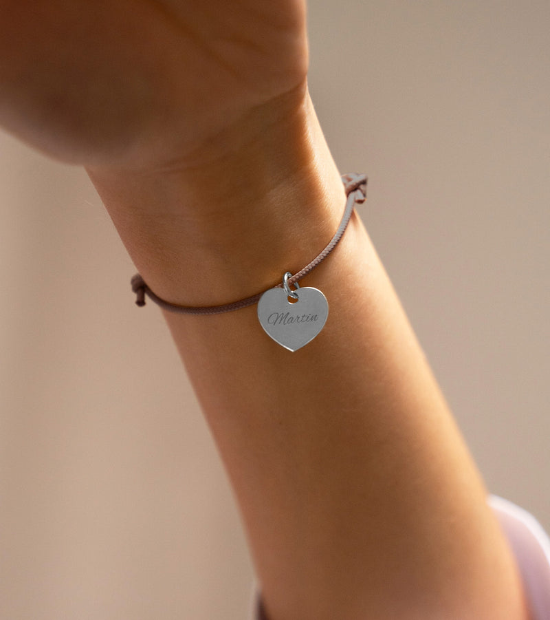 Une représentation visuelle d'un bracelet coeur argenté, de 15mm, avec un cordon en marron clair, personnalisable.