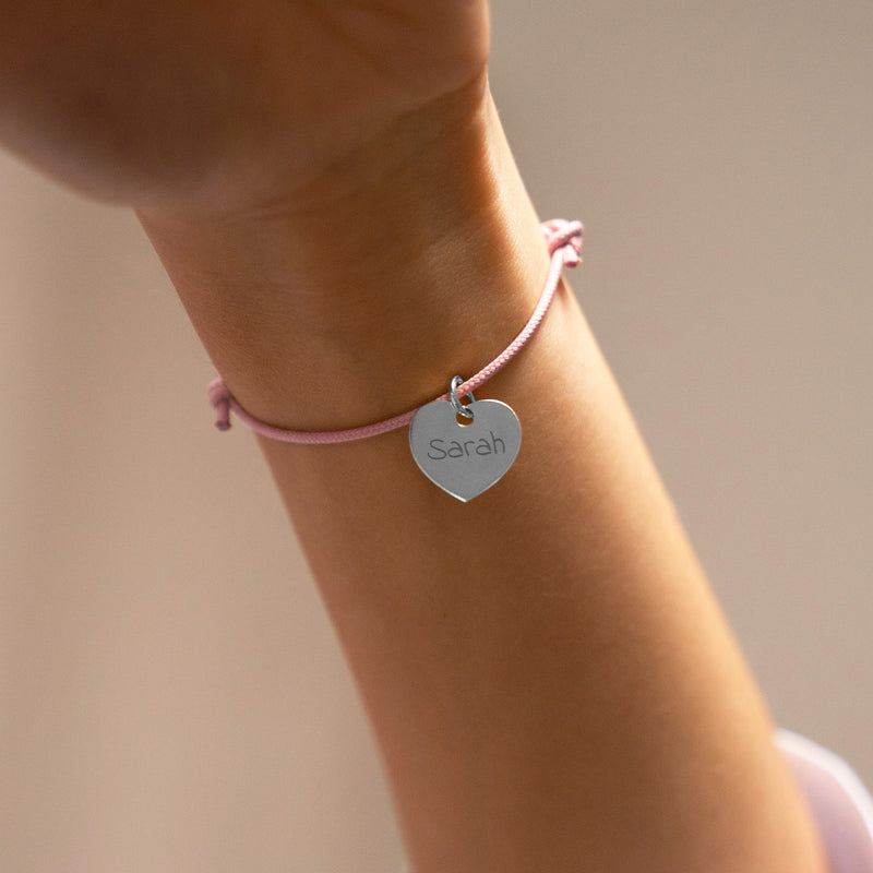 Ce bracelet argenté en forme de cœur mesure 15mm de diamètre, accroché à un cordon rose.