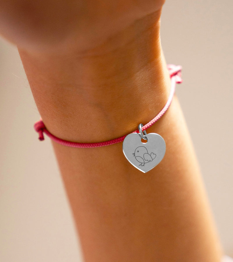 Découvrez ce bracelet argenté avec un cœur et un cordon rose fuchsia.