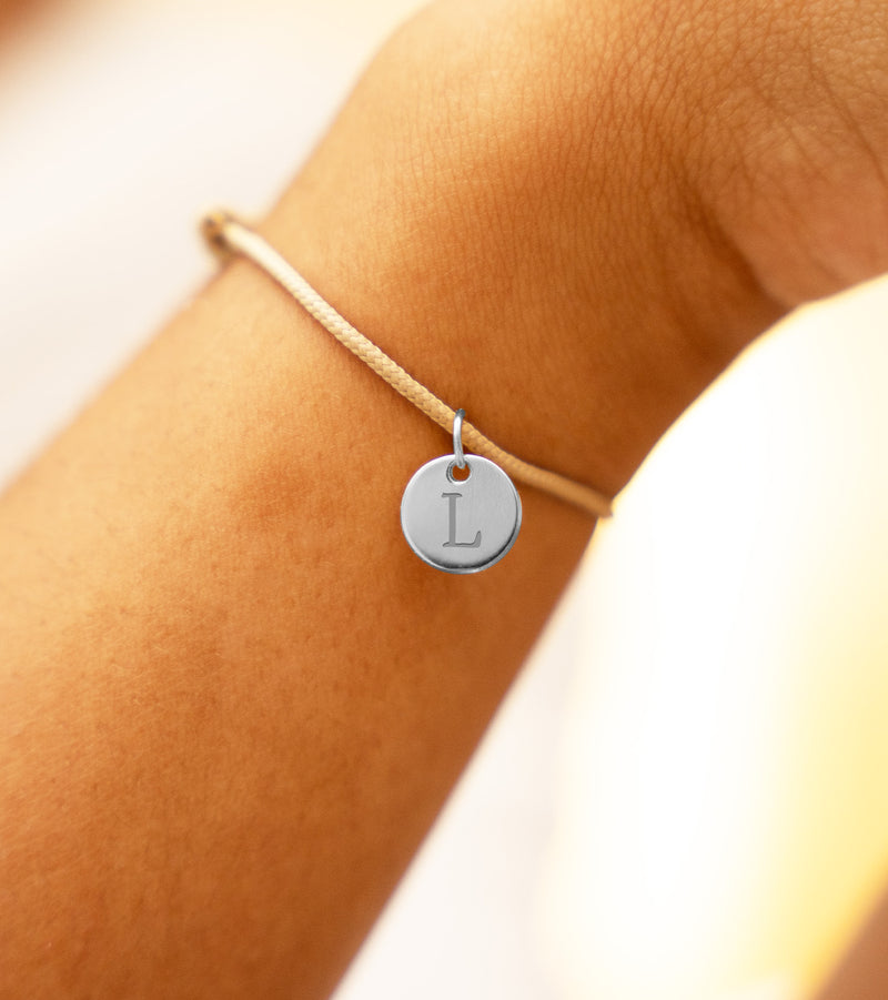 Bracelet en argent orné d'une médaille de 10mm sur cordon beige.