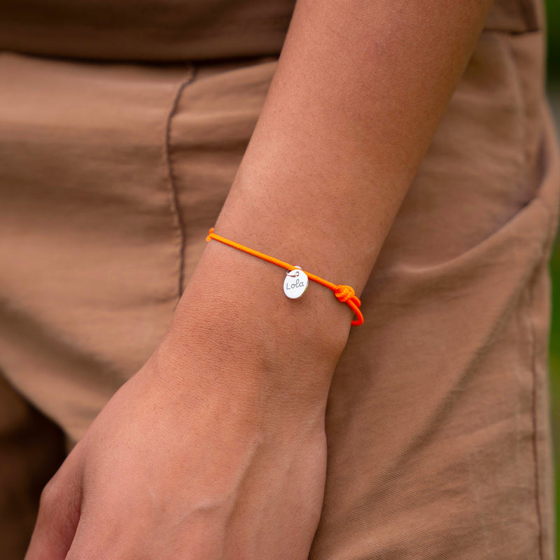 Un bijou unique. Bracelet personnalisé avec une médaille en argent de 10mm et un cordon orange fluo.
