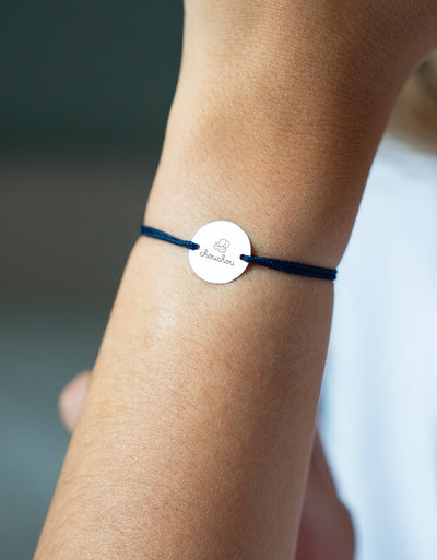 Médaille argentée de 15mm, suspendue à un bracelet, rehaussée d'un cordon bleu marine.