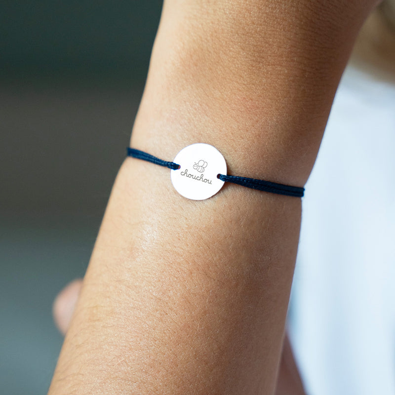 Médaille argentée de 15mm, suspendue à un bracelet, rehaussée d'un cordon bleu marine.