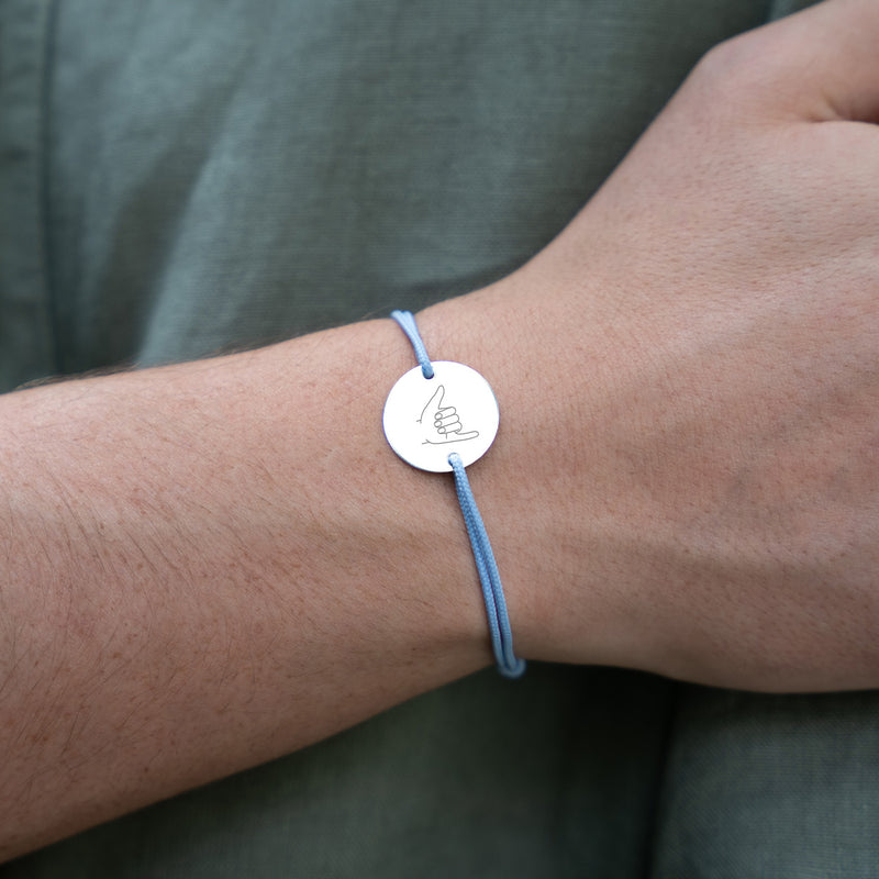 Sur fond de cordon bleu pastel, un bracelet en argent accueille une médaille de 15mm personnalisée avec deux trous.