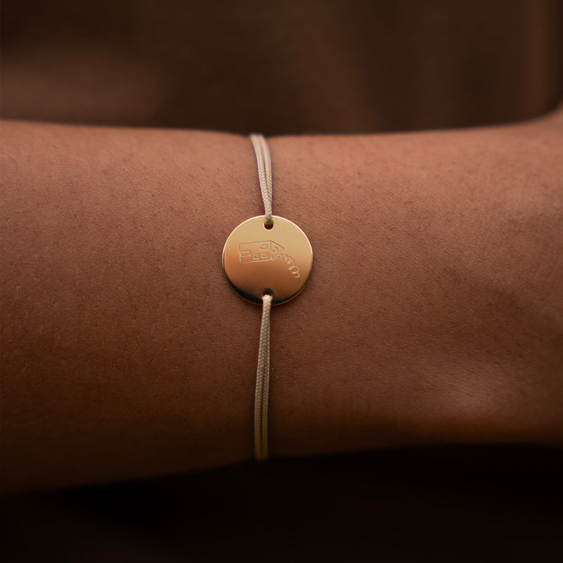 Un bracelet personnalisé, orné d'une médaille plaquée or de 15mm et de deux trous, complété par un cordon beige.