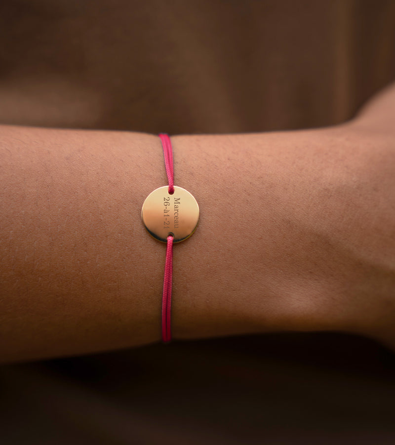 Médaille de 15mm plaquée or, deux trous pour fixation, sur un bracelet personnalisé en cordon rose fuchsia.