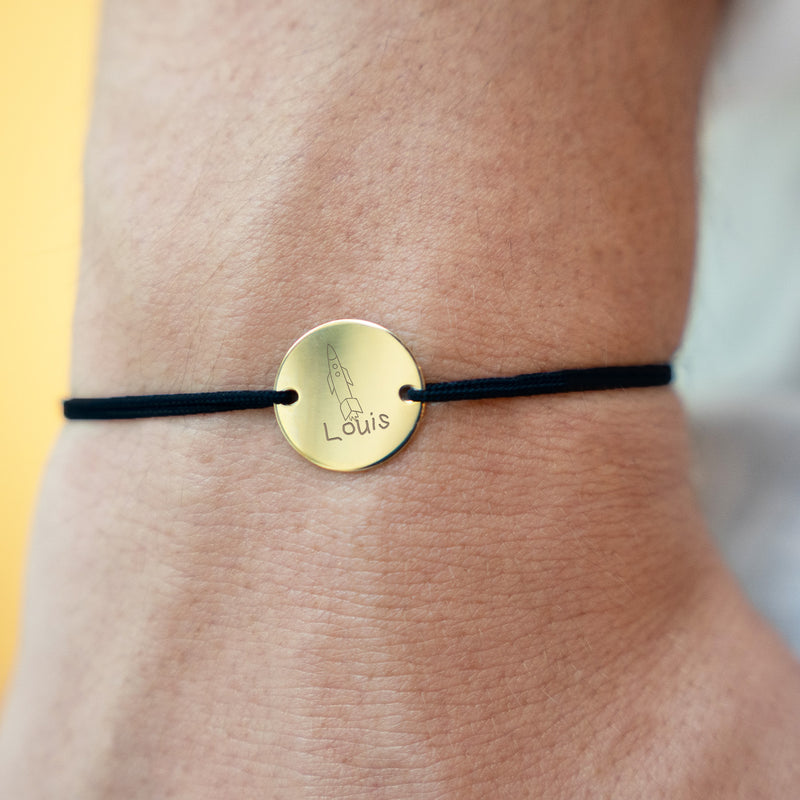 Un bracelet élégant, orné d'une médaille personnalisée de 15mm en plaqué or et accompagné d'un cordon noir.