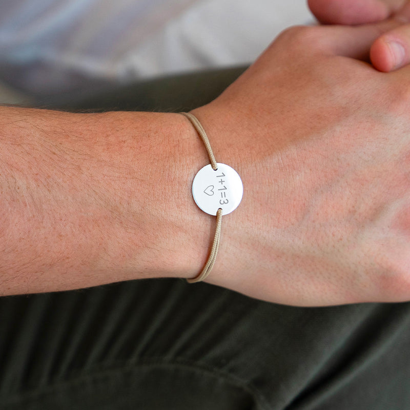 Un bracelet argenté avec une médaille de 15mm à personnaliser, complété par deux trous pour un cordon beige.