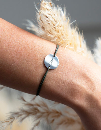 Bracelet argenté au cordonkaki, orné d'une médaille personnalisée de 15mm et de deux trous distinctifs.