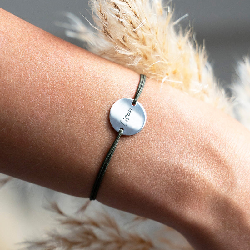Bracelet argenté au cordonkaki, orné d'une médaille personnalisée de 15mm et de deux trous distinctifs.