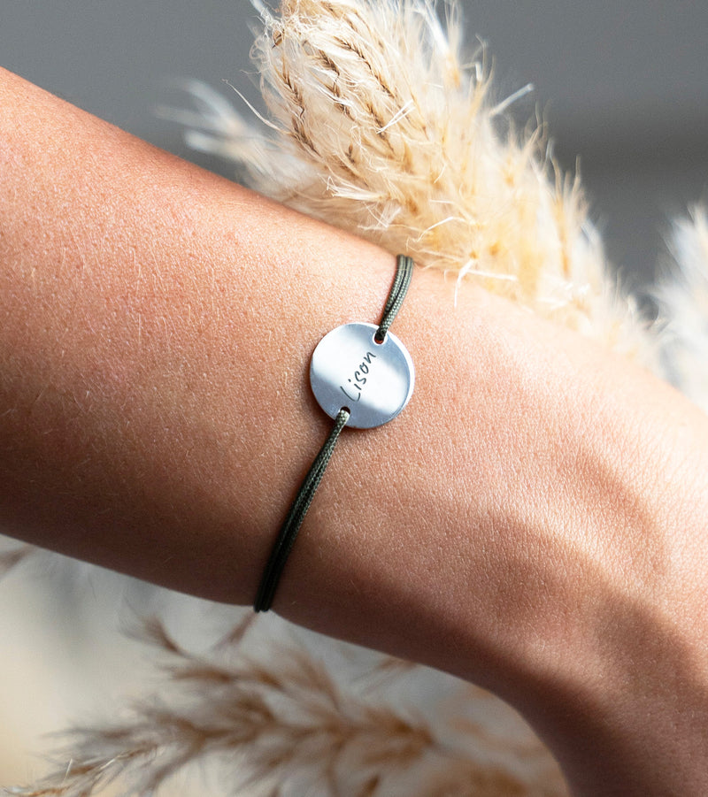 Bracelet argenté au cordonkaki, orné d'une médaille personnalisée de 15mm et de deux trous distinctifs.