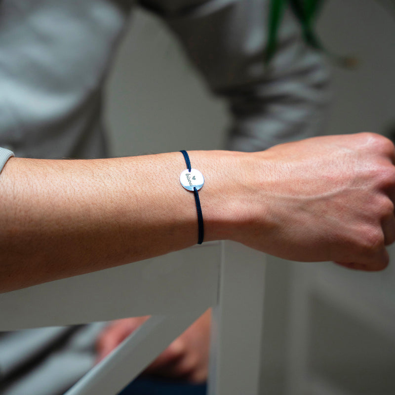 Un bracelet argenté de 15mm, orné d'une médaille personnalisée et rehaussé d'un cordon bleu marine.