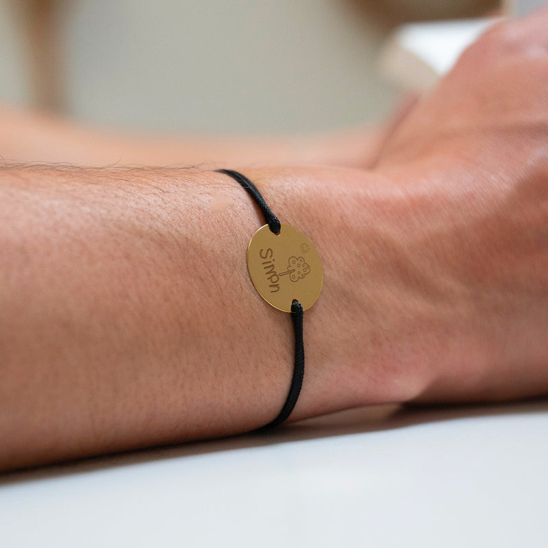 Un bracelet personnalisé avec une médaille en 20mm, deux trous en plaqué or, et un cordon noir pour une touche d'élégance.