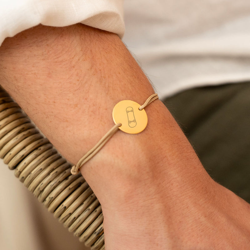 Un bracelet unique avec une médaille de 20mm, deux trous en plaqué or et un cordon beige, parfait pour exprimer votre style.