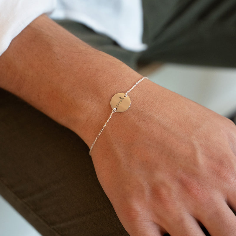 Une médaille personnalisée de 15mm suspendue à un bracelet en argent, deux trous assurent sa fixation. La chaîne plate offre une élégance discrète à ce bijou unique.