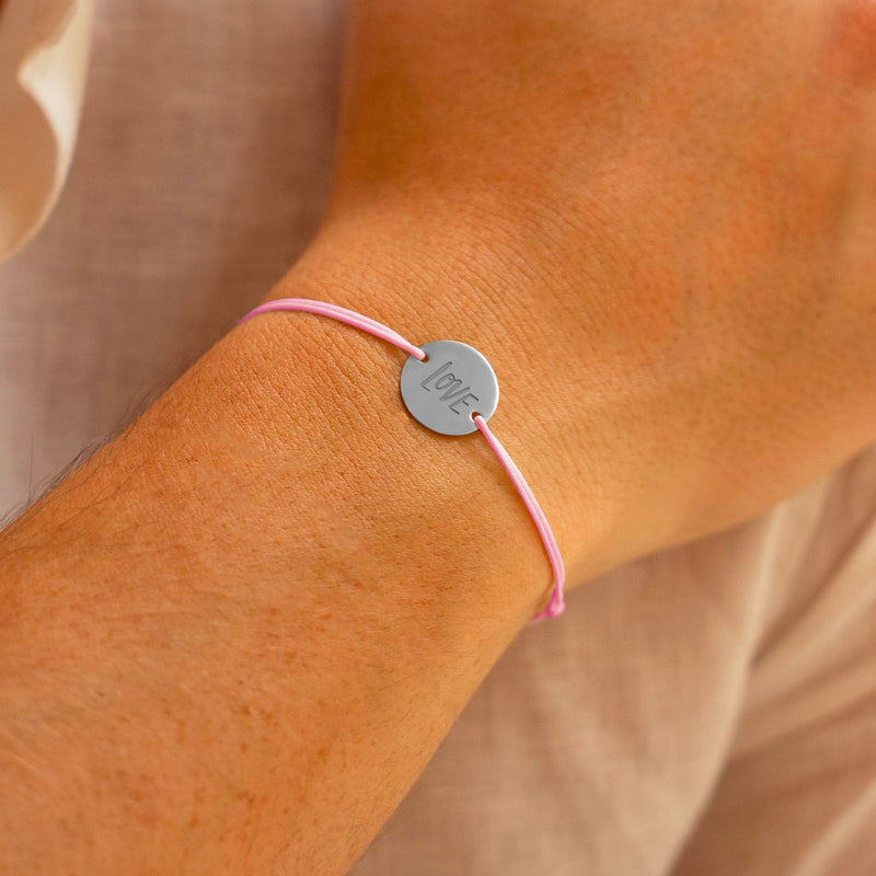 Un bracelet argenté lumineux, orné d'une médaille de 15mm personnalisée munie de 2 trous, associé à un cordon rose charmant