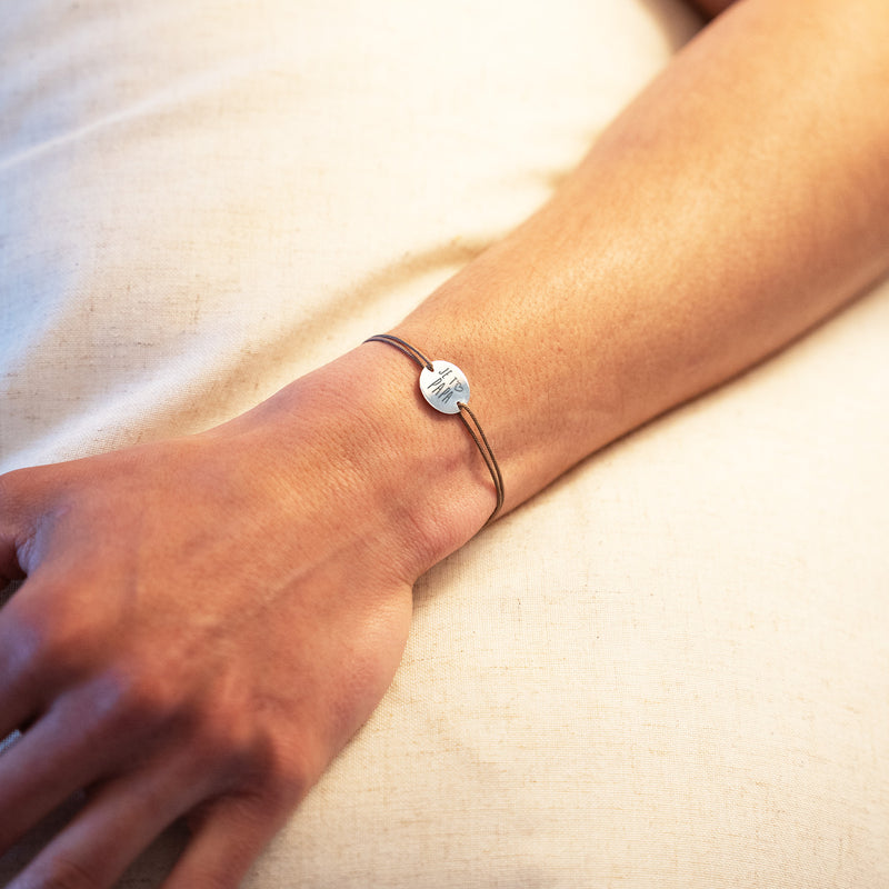 Une pièce argentée, accompagnée d'une médaille de 15mm personnalisée et de deux trous pour le cordon marron clair. Un accessoire raffiné et intemporel pour toutes les occasions.