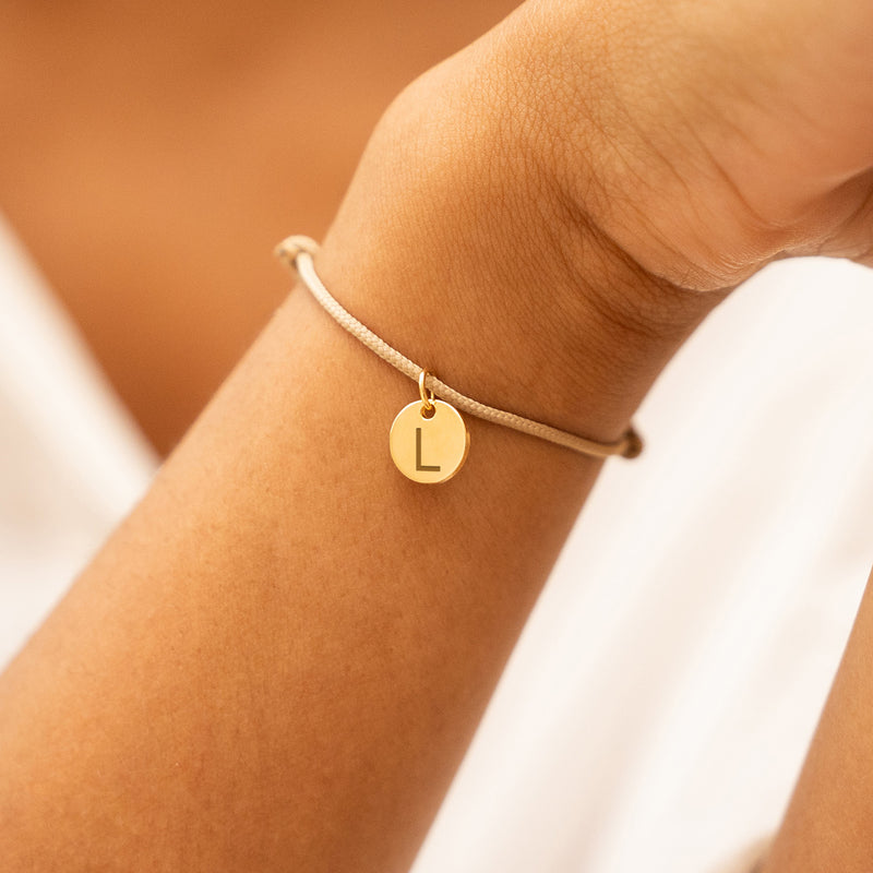 Cordon beige orné d'une médaille plaquée or 10mm, un bracelet unique pour compléter votre tenue.