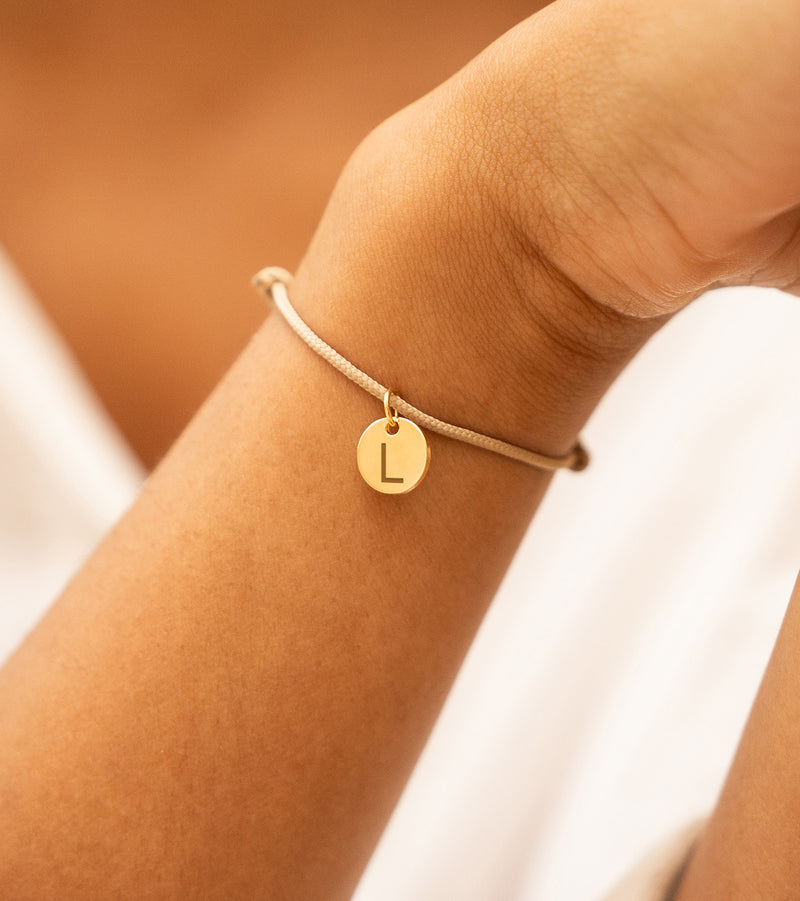 Cordon beige orné d'une médaille plaquée or 10mm, un bracelet unique pour compléter votre tenue.