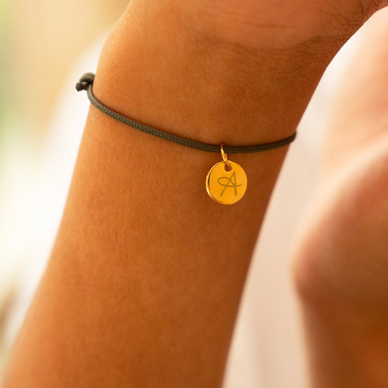 Un bracelet en cordon kaki avec une médaille plaquée or de 10mm, personnalisable à votre nom.