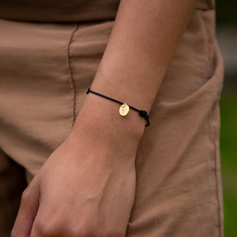 Bracelet en plaqué or avec médaille de 10mm, subtil et chic, rehaussé par un cordon noir pour une touche de modernité.
