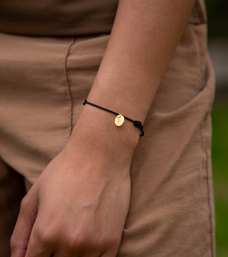 Bracelet en plaqué or avec médaille de 10mm, subtil et chic, rehaussé par un cordon noir pour une touche de modernité.