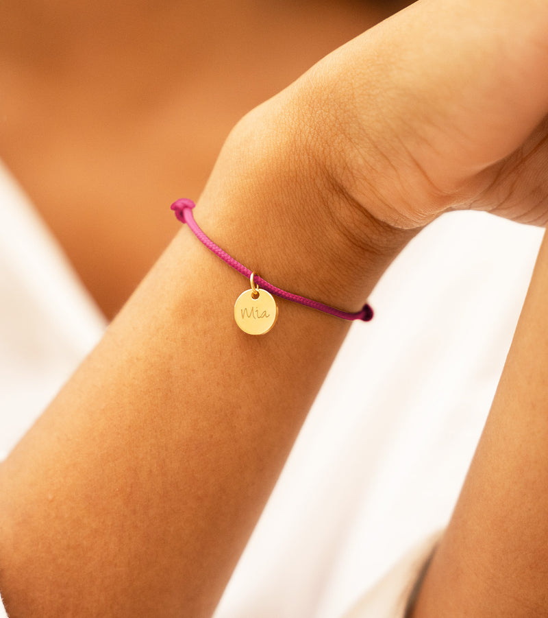 Un bracelet en cordon rose fuchsia avec une médaille plaquée or de 10mm, personnalisable.
