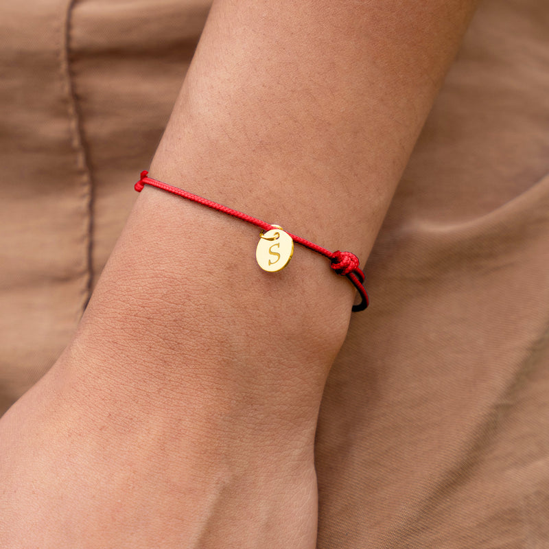 Un bracelet en cordon rouge orné d'une médaille plaquée or de 10mm, un accessoire chic pour votre poignet.
