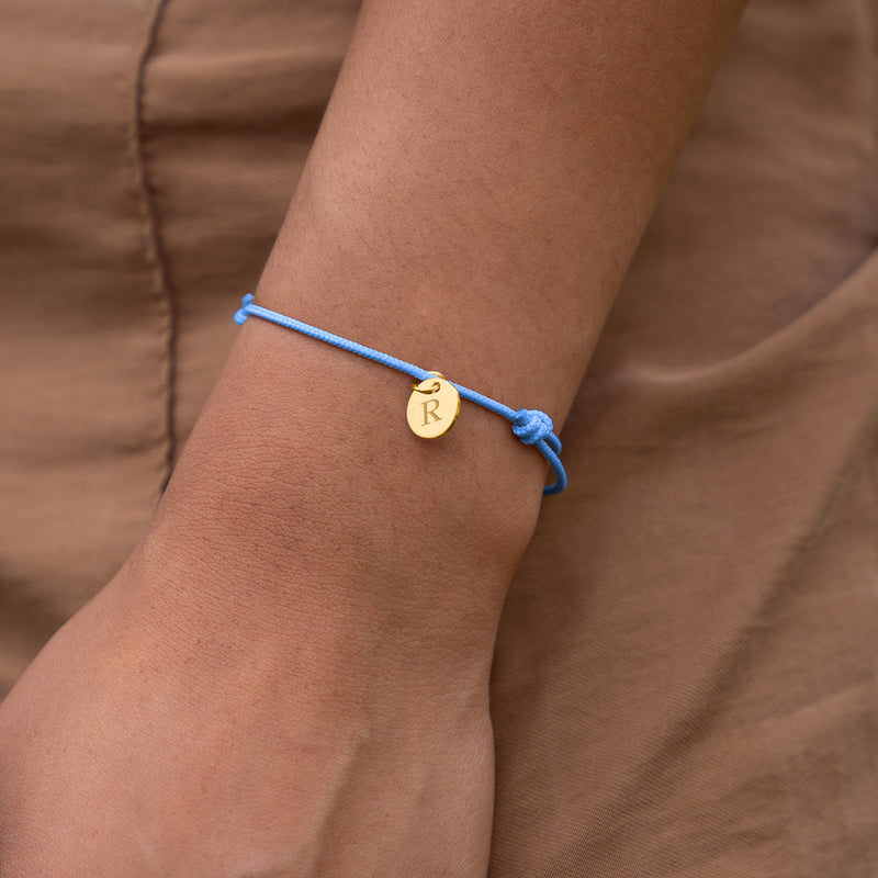 Un magnifique bracelet en plaqué or avec une médaille de 10mm, attaché à un cordon bleu pastel.