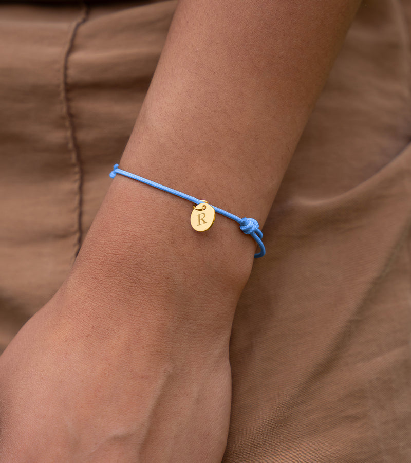 Un magnifique bracelet en plaqué or avec une médaille de 10mm, attaché à un cordon bleu pastel.