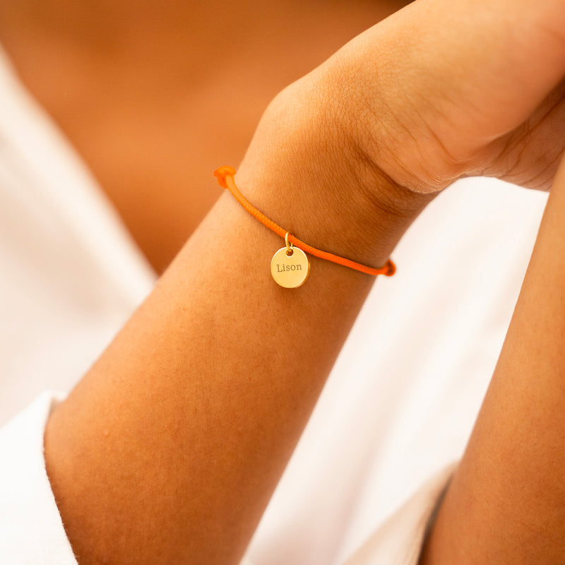 Un bracelet composé d'une médaille dorée de 10 mm et d'un cordon orange fluo.