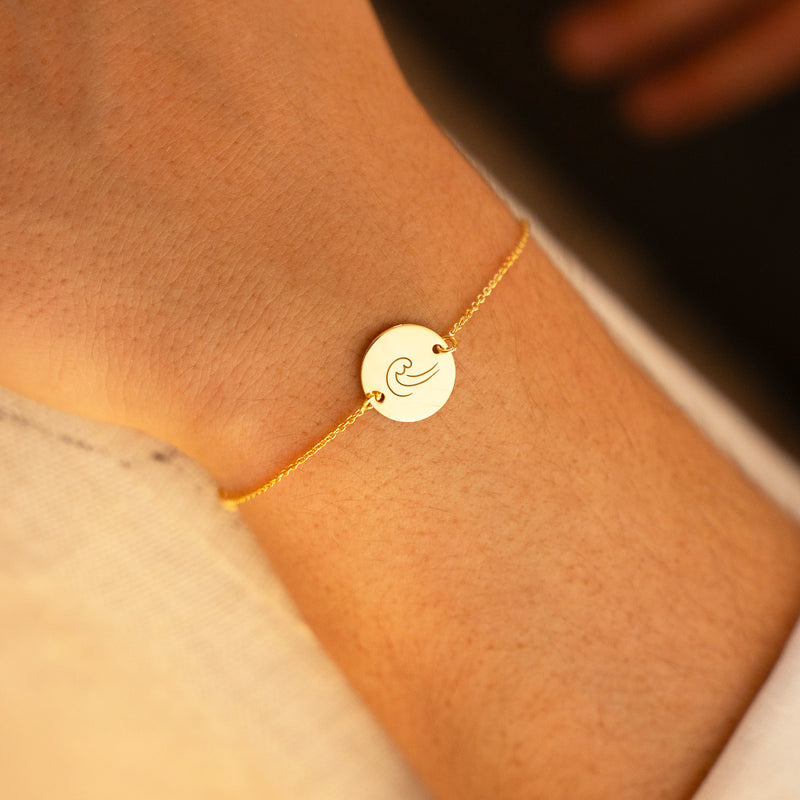 Bracelet en plaqué or, agrémenté d'une médaille de 15mm dotée de deux trous, suspendue à une chaîne maille.