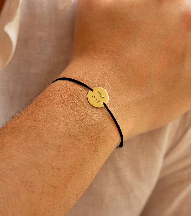 Bracelet, agrémenté d'une médaille personnalisée de 15mm en plaqué or et d'un cordon noir.