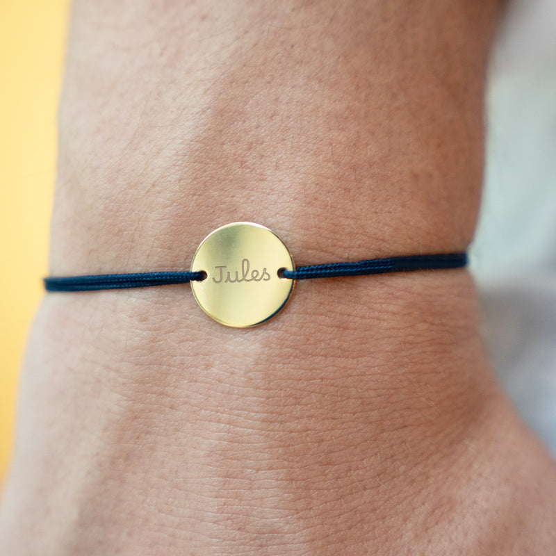 Un bracelet sur mesure, orné d'une médaille plaquée or de 15 mm, percée de deux trous, sur un cordon bleu marine.