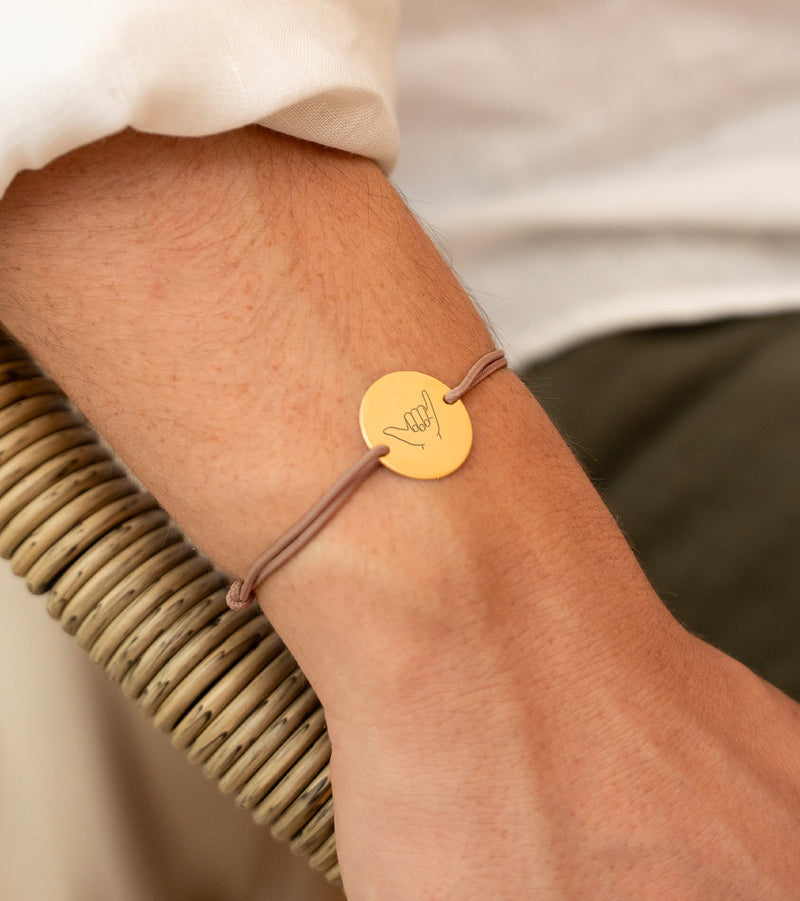 une médaille personnalisée en 20mm, ce bracelet est doté de deux trous en plaqué or et d'un cordon marron clair.