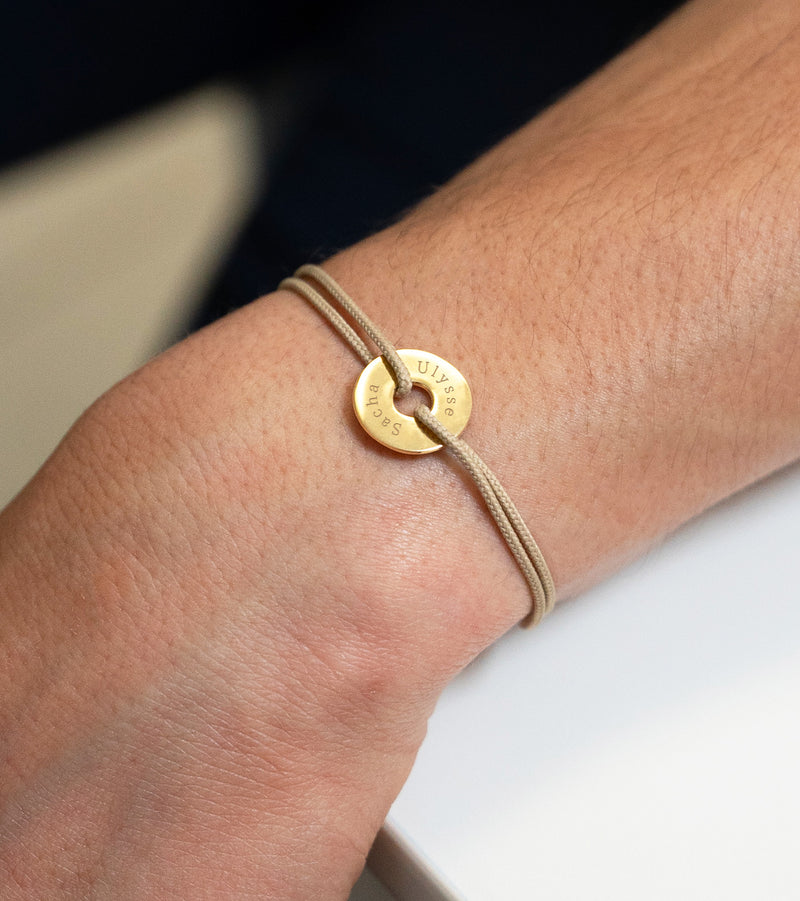 En forme de cible et avec un cordon beige, ce bracelet personnalisé en 15mm est plaqué or